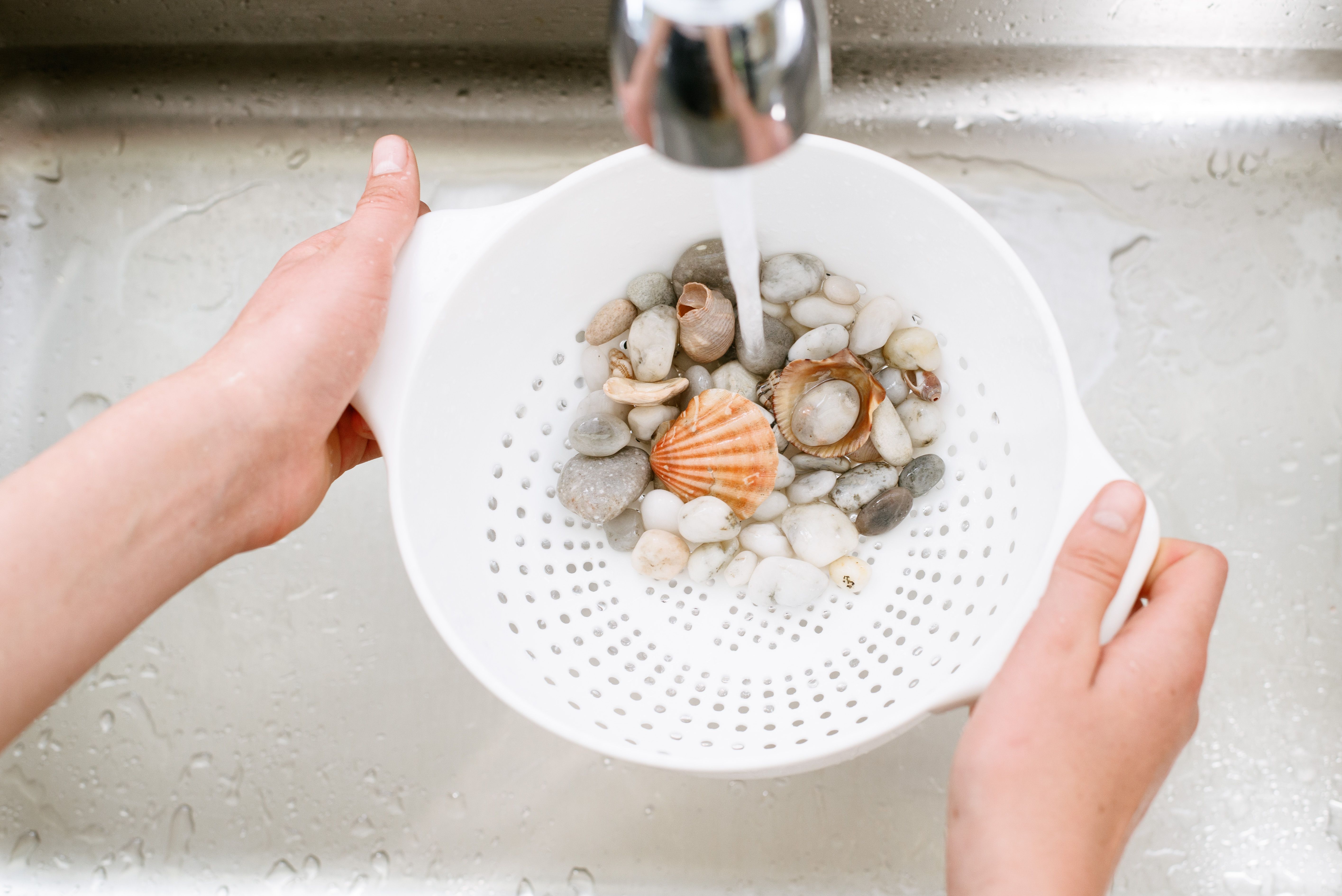 Décorations de bol à poisson rincées sous robinet de course avec de l'eau tiède et une passoire blanche